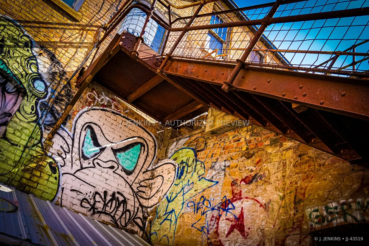 Rusting steel staircase above layered graffiti