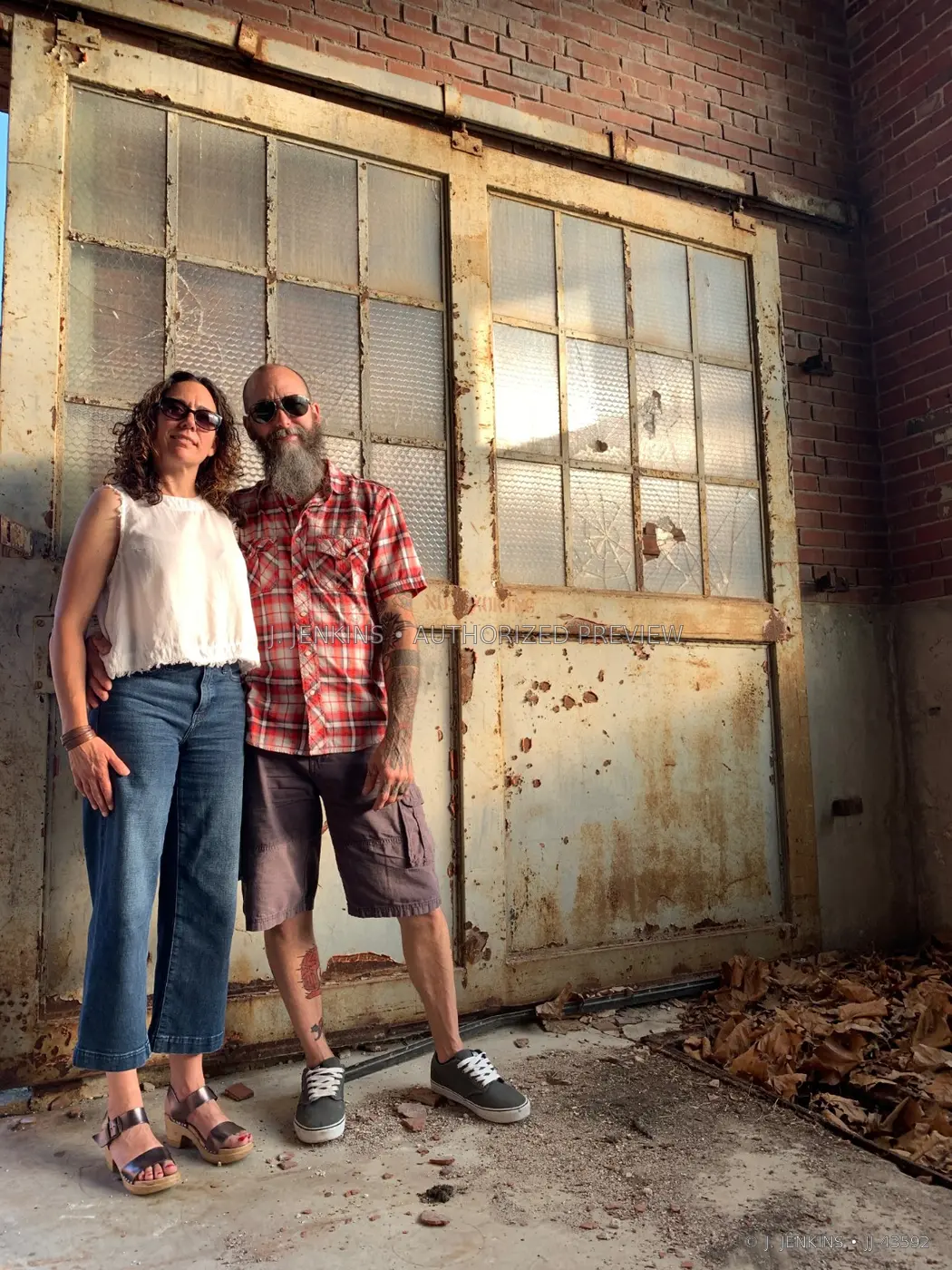 Couple standing in warm light before weathered industrial doors