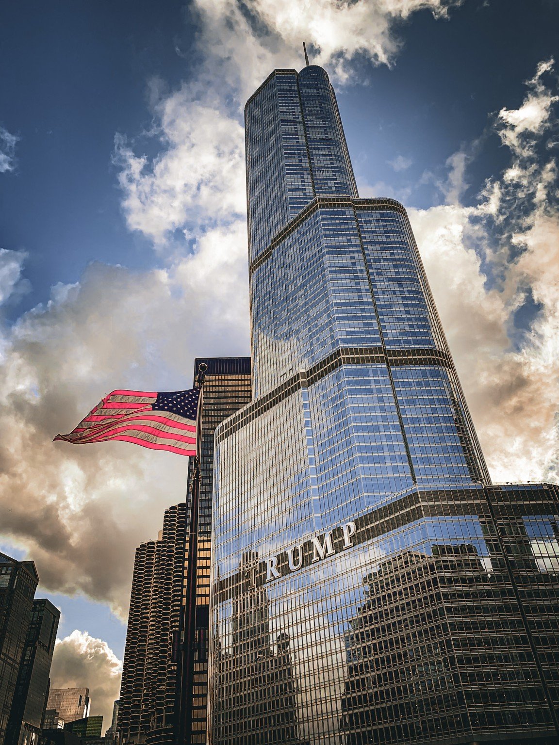 American flag moving before a reflective Chicago skyscraper beneath luminous clouds
